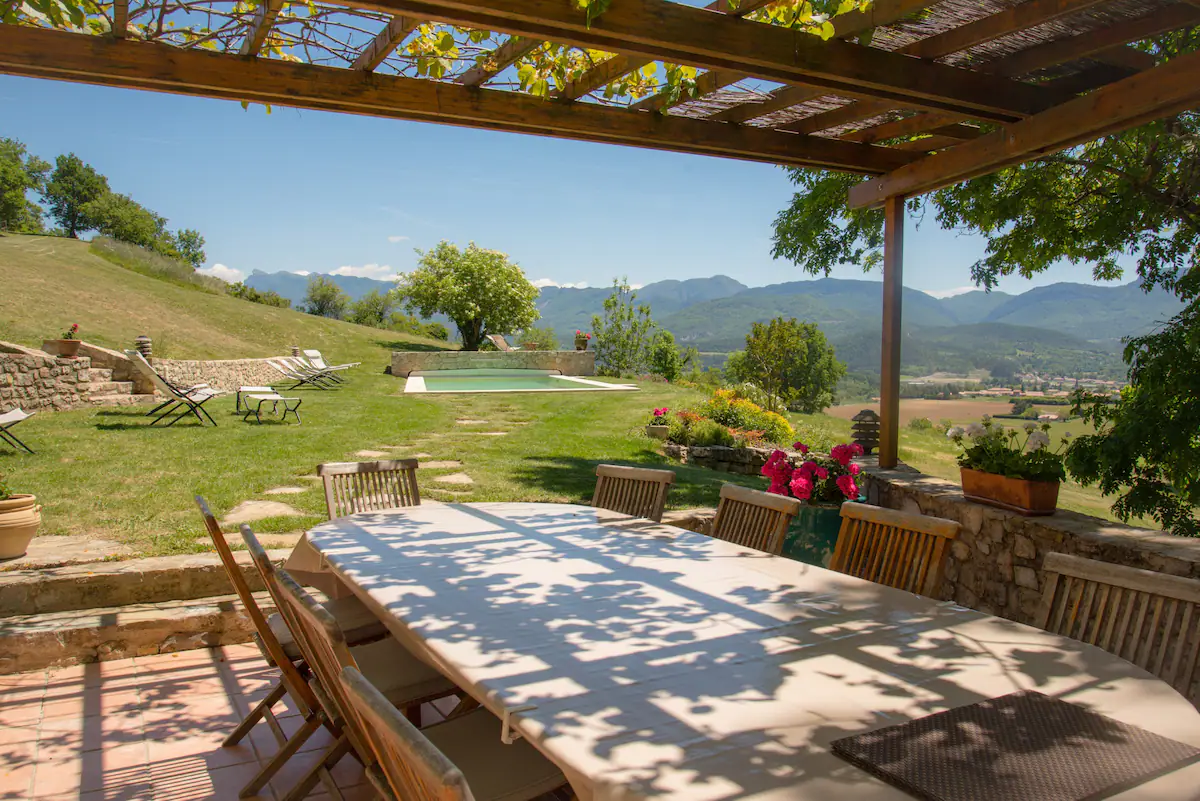 Terrasse ombragée sous la pergola, table dressée face à la piscine et aux montagnes